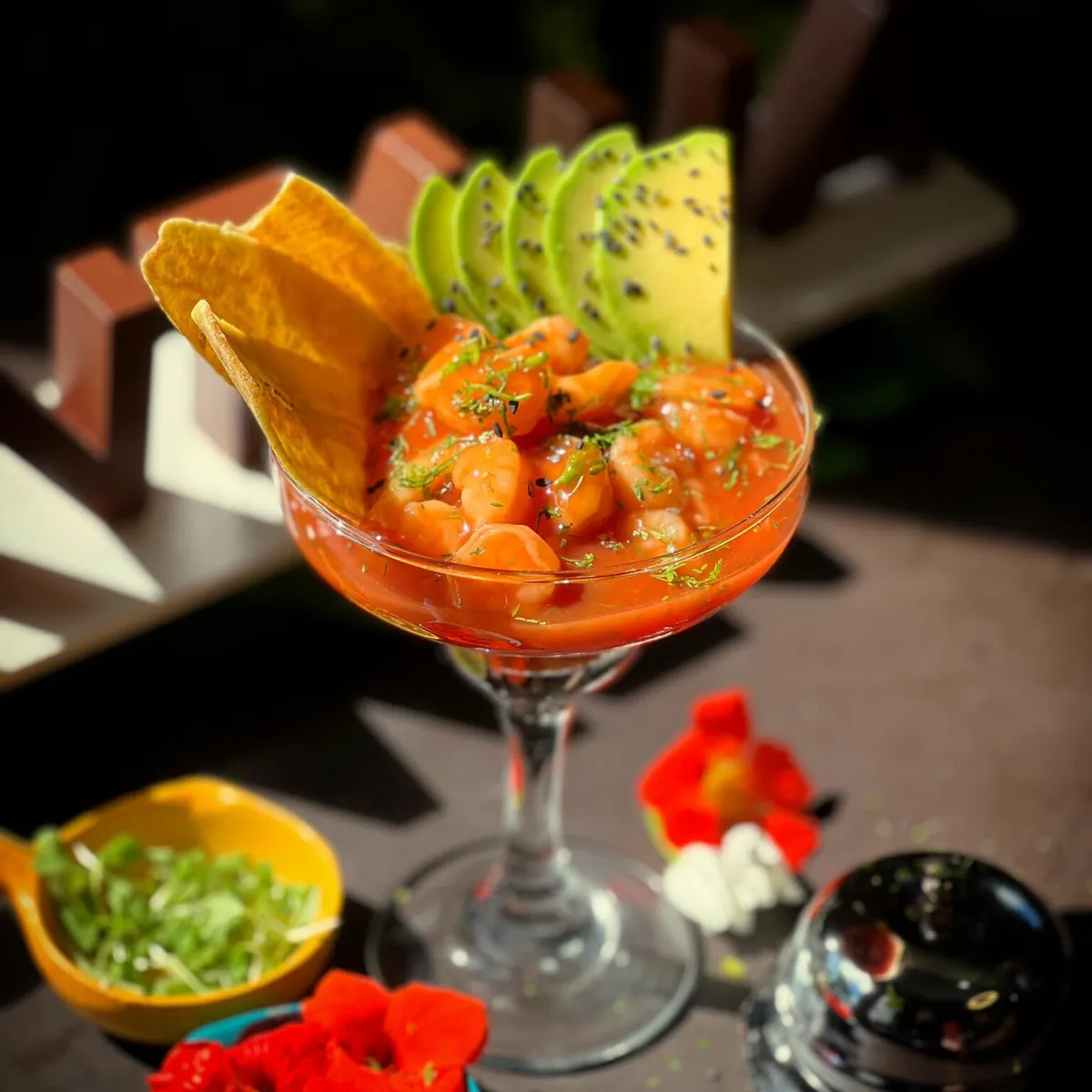 Cóctel de camarón de Santana servido en copa, con abanico de aguacate, chips de plátano y flores comestibles